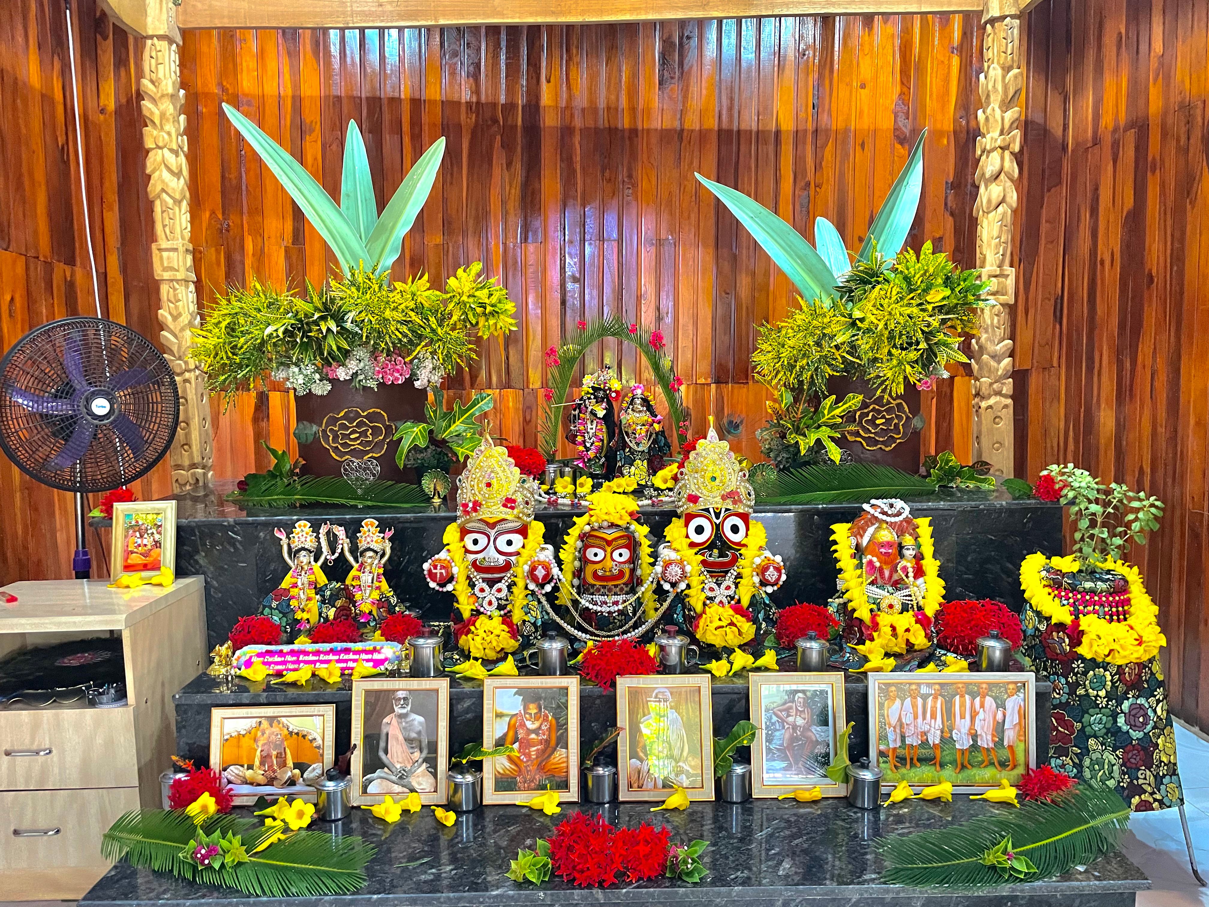The main altar at ISKCON Kumasi, featuring the beautifully decorated deities of Jagannath, Baladeva, Subhadra, Gaura Nitai, and Radha Krishna, surrounded by flowers and pictures of the acharyas.